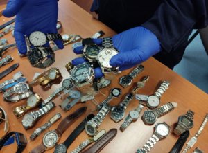 policjant trzyma w rękach skradzione zegarki, w tle pozostałe zegarki leżące na stole