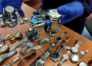 policjant trzyma w rękach skradzione zegarki, w tle pozostałe zegarki leżące na stole