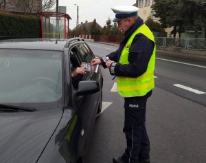 policjant ruchu drogowego rozmawia z kierowcą i wręcza mu ulotkę