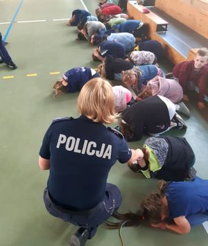 policjantka pokazuje grupie dzieciom jak zachować się w kontakcie z agresywnym zwierzęciem